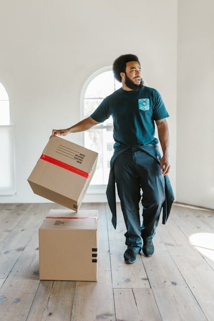 A professional removal team from Brent Movers is engaged in the home relocation process inside a bright, spacious room with large arched windows allowing natural daylight to illuminate the space. One